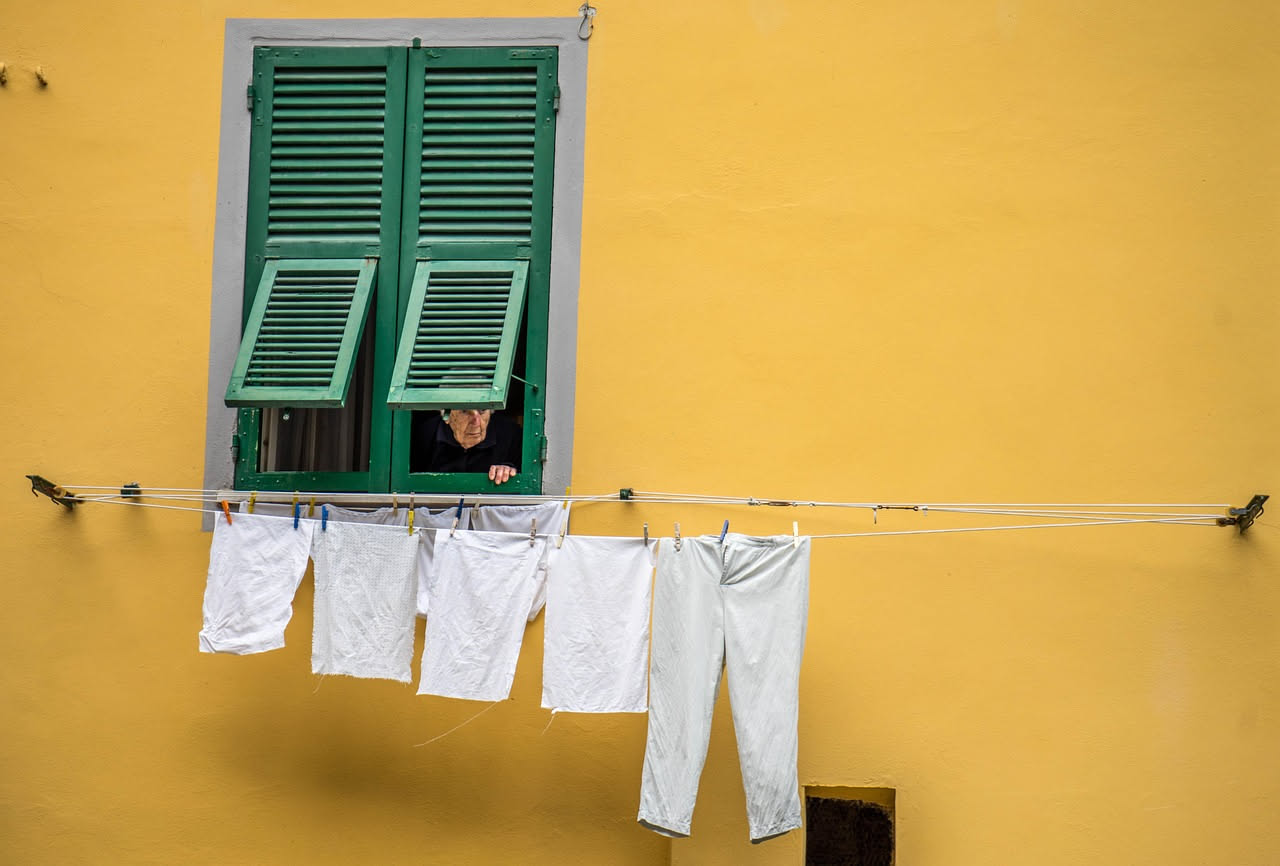 Finestra di appartamento italiano con davanzale bianco, due stracci e una bottiglia di aceto bianco accanto a un giornale, sole che entra dalla finestra pulita