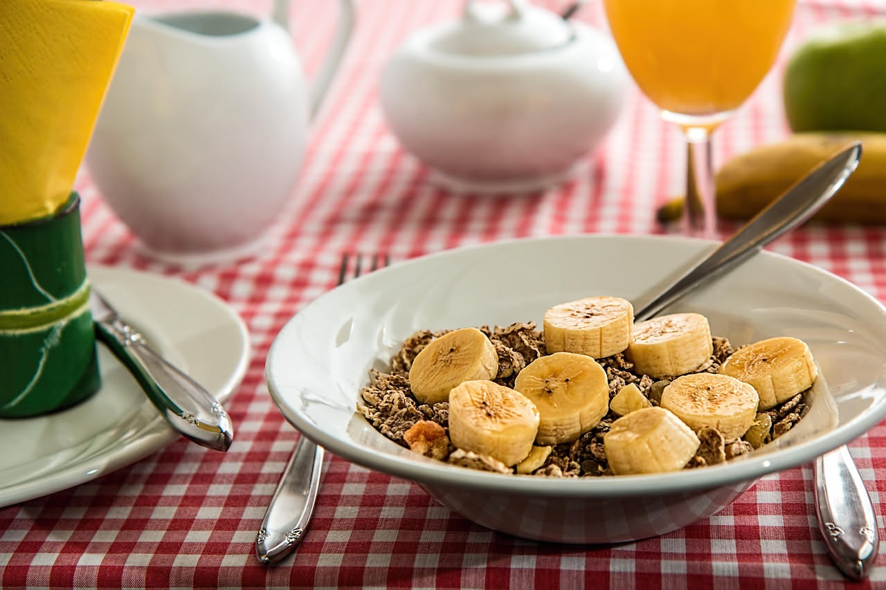 Tavolo da colazione con pane integrale tostato, burro, miele, yogurt greco, frutti di bosco, uova strapazzate e una tazza di caffè nero su uno sfondo bianco