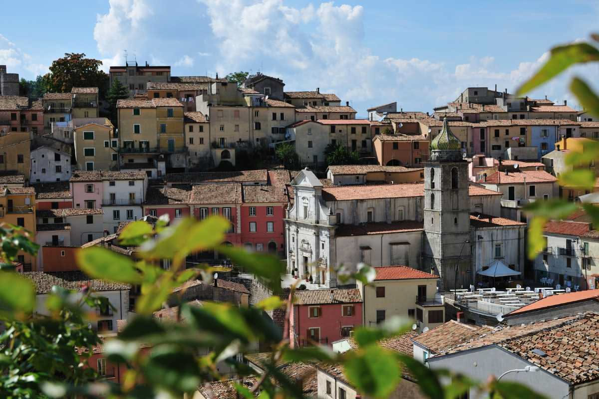 Piazza principale di Pescocostanzo con la chiesa al centro, edifici in pietra medievale, vicoli stretti e montagne innevate sullo sfondo