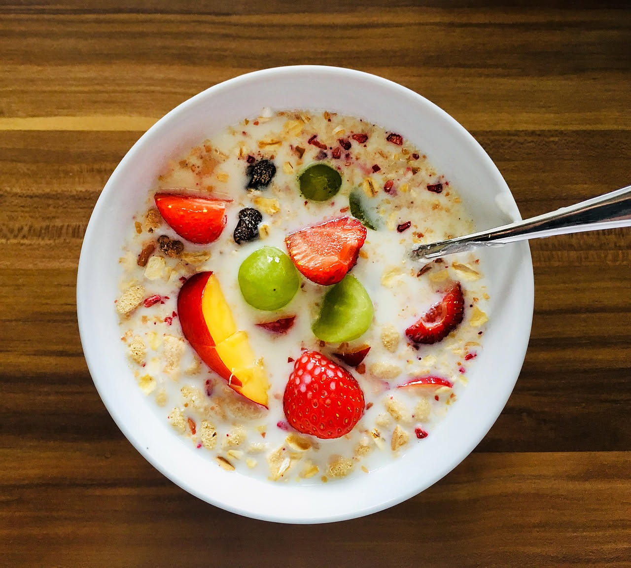 Colazione equilibrata con uova strapazzate, yogurt naturale, pane integrale tostato, fragole fresche e un bicchiere di latte su tavolo di legno chiaro