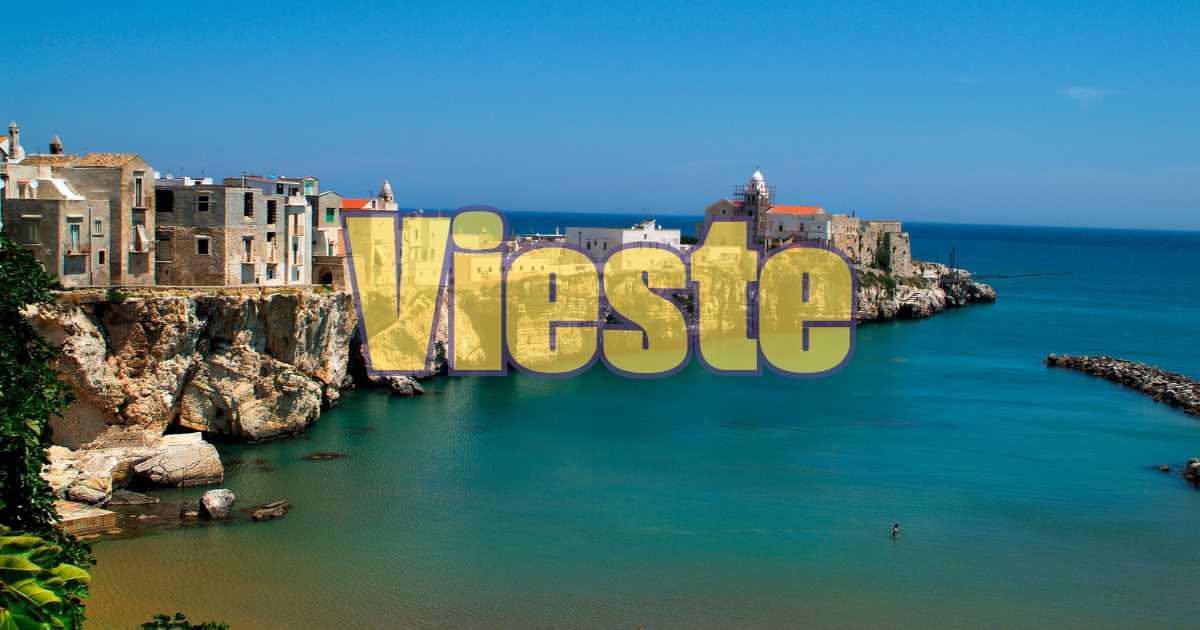 Vista panoramica di Vieste con case bianche arroccate sulla roccia, faraglioni gialli nel mare azzurro e spiaggia sabbiosa sottostante